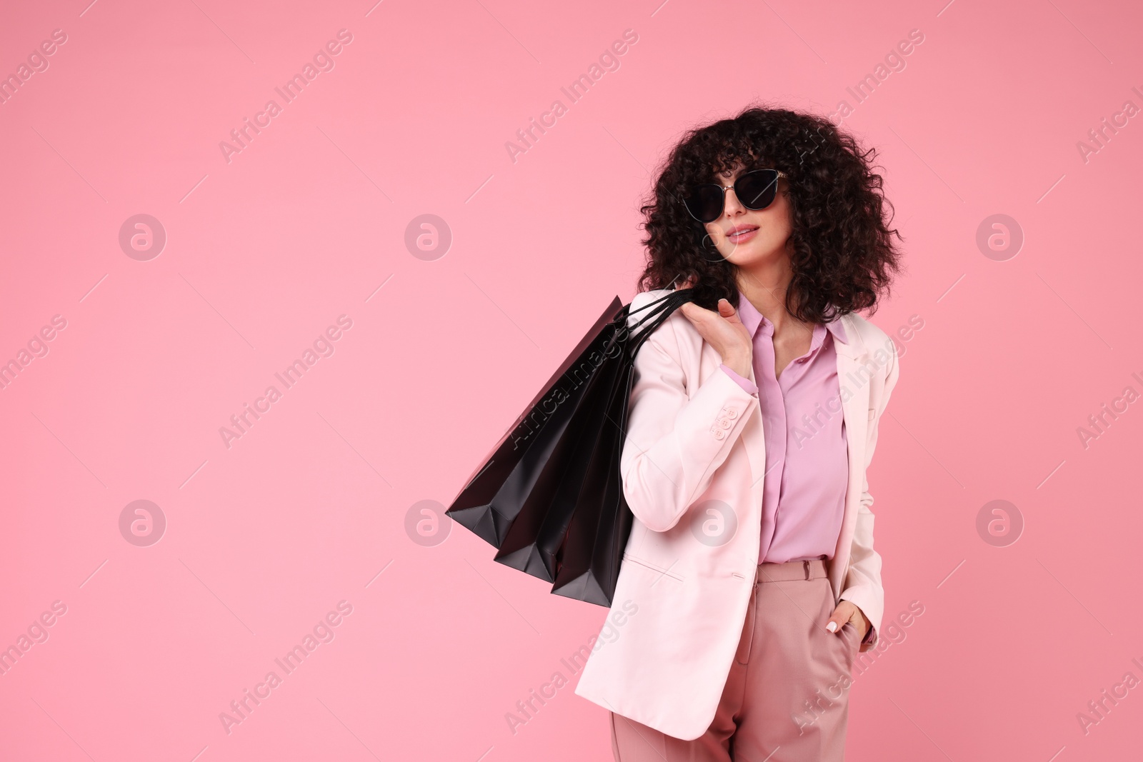 Photo of Happy young woman with shopping bags and stylish sunglasses on pink background. Space for text