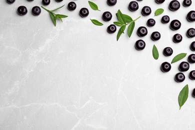 Photo of Fresh acai berries with leaves on light stone table, flat lay. Space for text