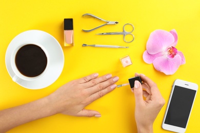 Woman applying nail polish on color background, top view