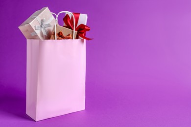 Photo of Pink paper shopping bag fullgift boxes on purple background. Space for text