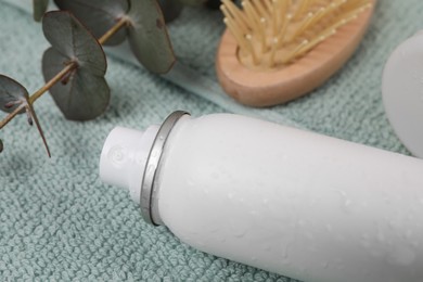 Photo of Dry shampoo spray, hairbrush and eucalyptus branch on towel, closeup