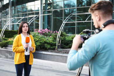 Photo of Young journalist and video operator working on city street