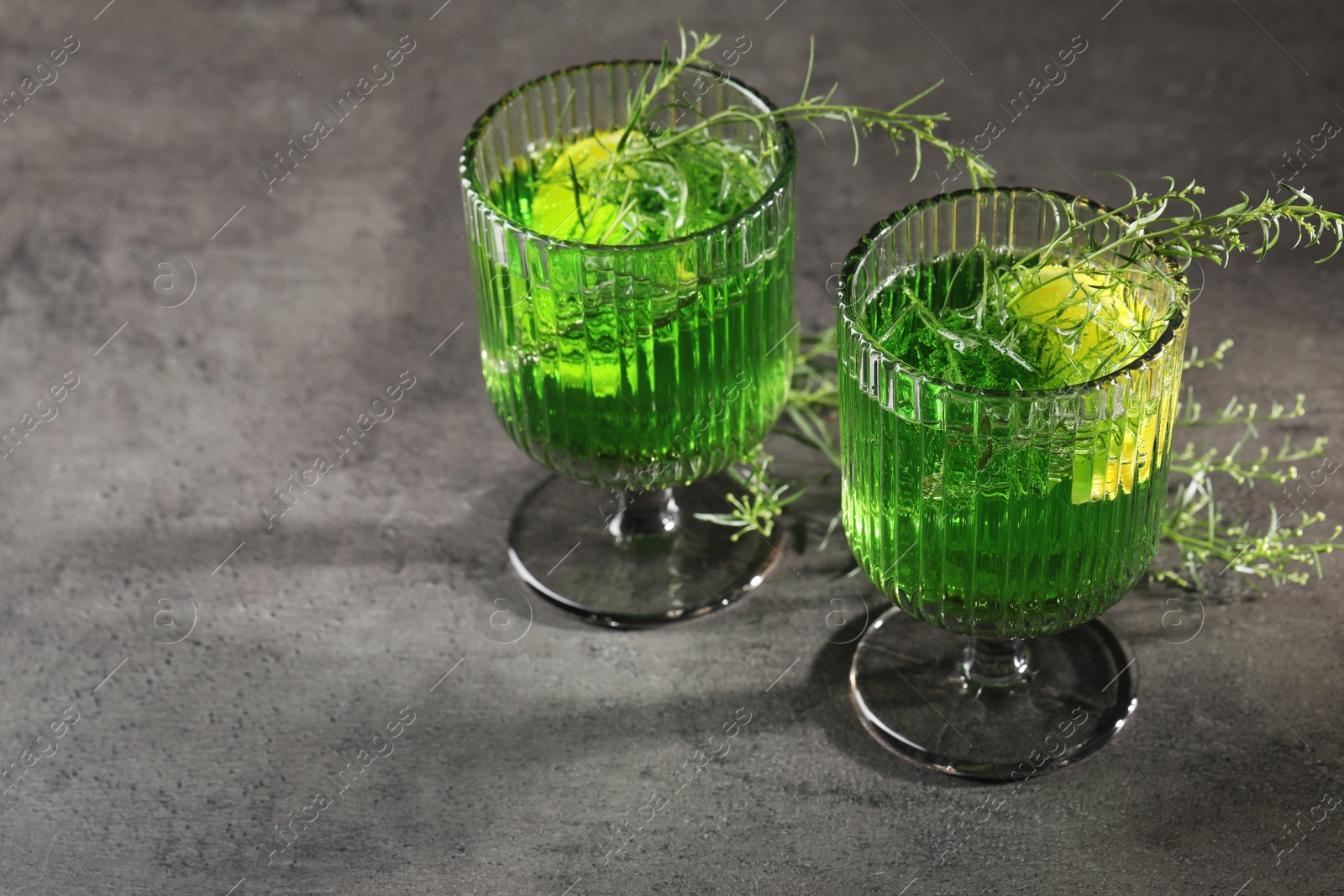 Photo of Glasses of homemade refreshing tarragon drink and sprigs on grey table, space for text