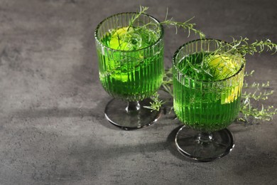 Photo of Glasses of homemade refreshing tarragon drink and sprigs on grey table, space for text