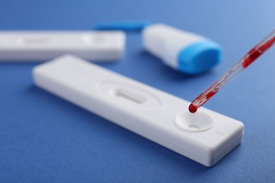 Photo of Dropping blood sample onto disposable express test cassette with pipette on blue background, closeup