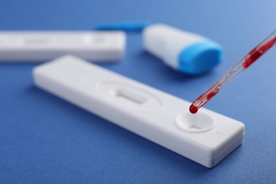 Dropping blood sample onto disposable express test cassette with pipette on blue background, closeup