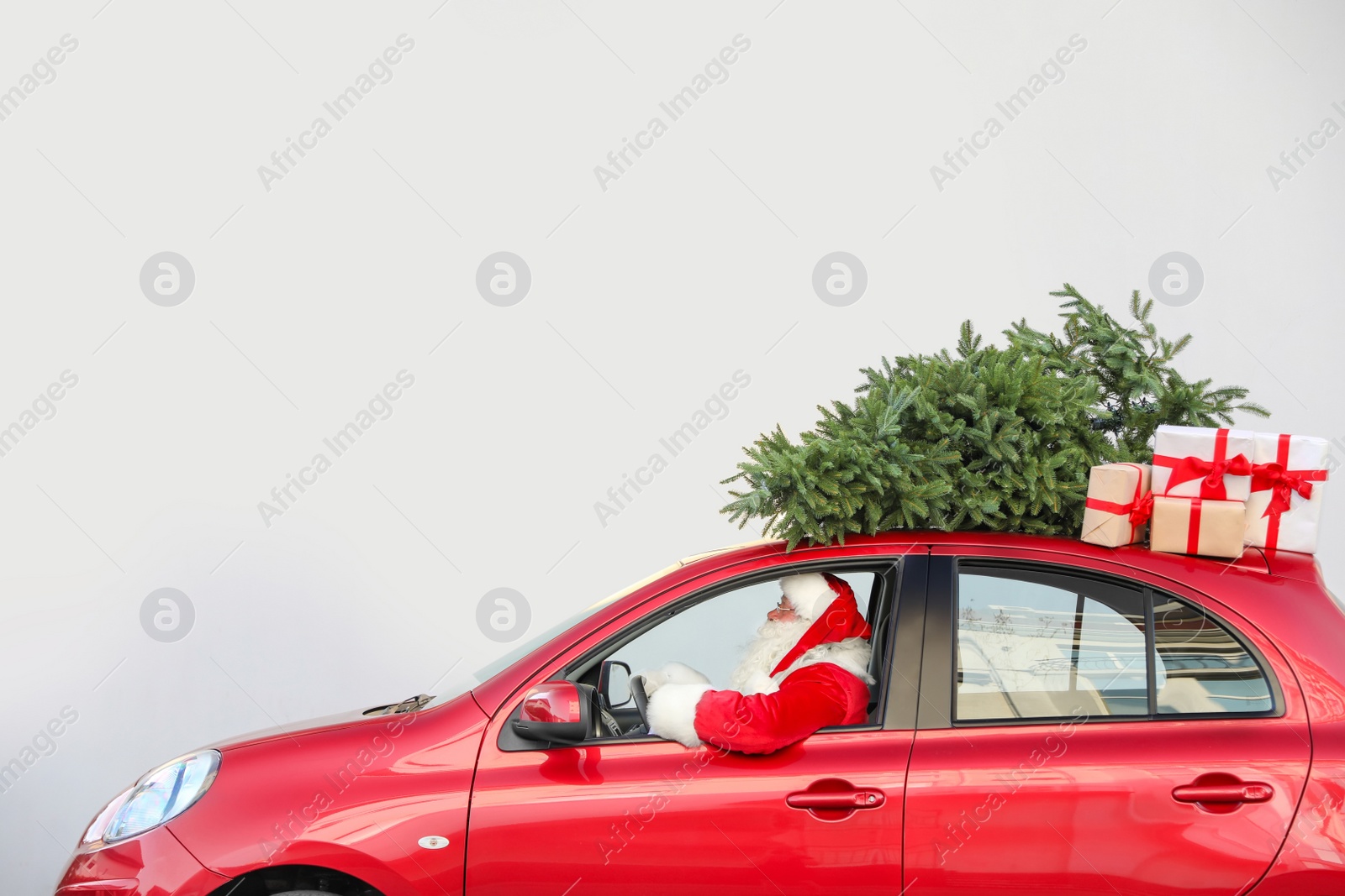 Photo of Authentic Santa Claus driving red car with gift boxes and Christmas tree, view from outside