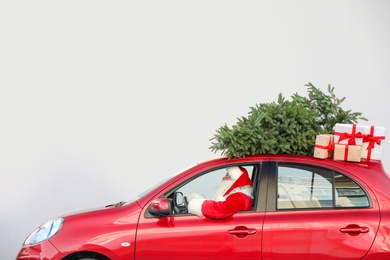 Authentic Santa Claus driving red car with gift boxes and Christmas tree, view from outside