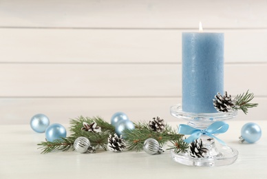 Photo of Glass candlestick with burning candle and Christmas decor on white wooden table. Space for text
