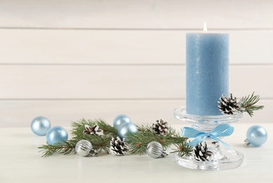 Glass candlestick with burning candle and Christmas decor on white wooden table. Space for text