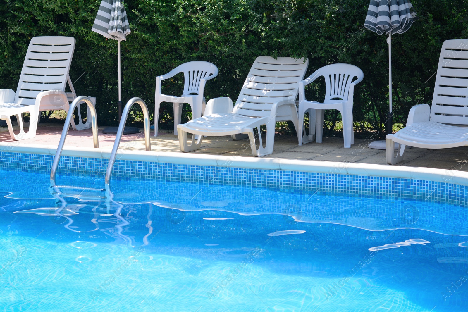 Photo of Swimming pool with deck chairs and umbrellas at resort on sunny day