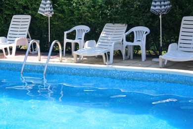 Photo of Swimming pool with deck chairs and umbrellas at resort on sunny day