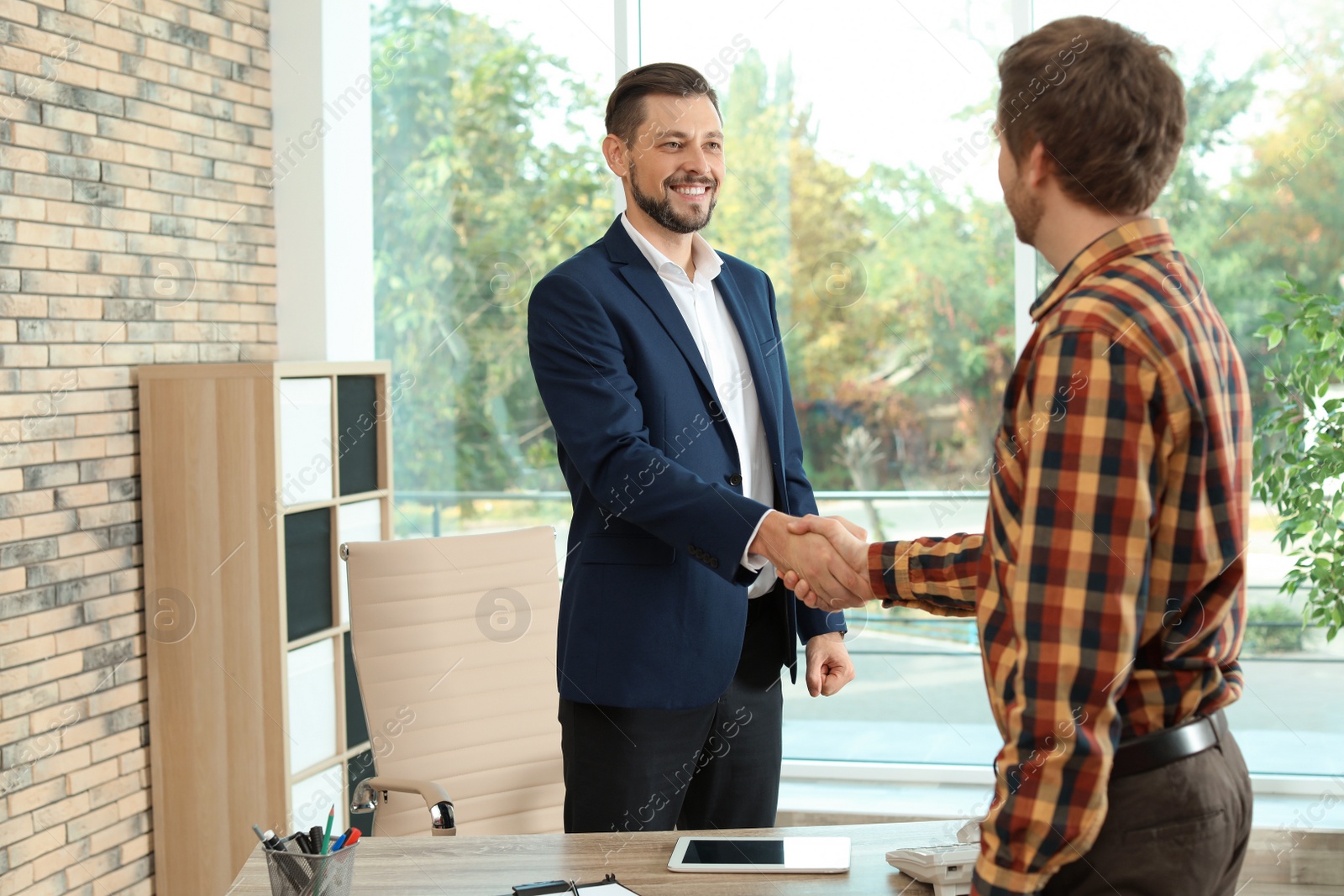 Photo of Human resources manager shaking hands with applicant during job interview in office