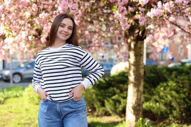 Beautiful woman near blossoming tree on spring day, space for text