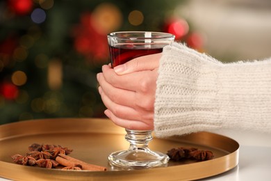 Woman holding glass cup of delicious mulled wine at white table against blurred background, closeup