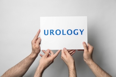 Men holding card with word UROLOGY on light background