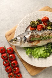 Delicious baked fish and vegetables on light grey table, top view