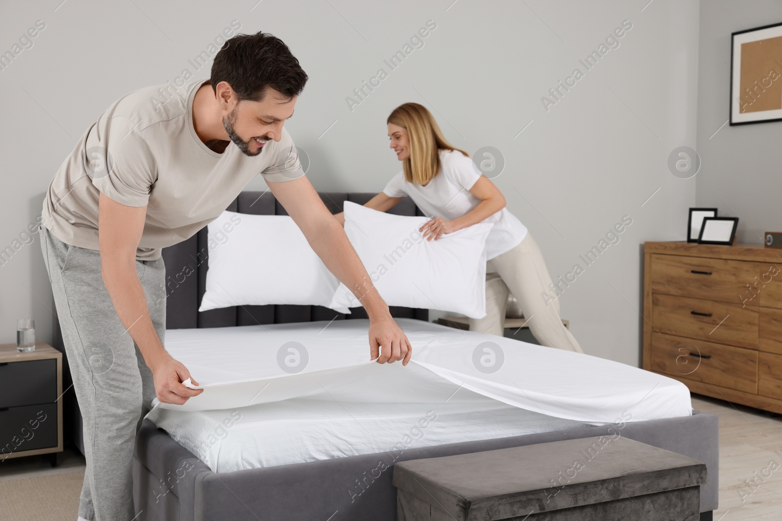 Photo of Couple changing bed linens in room. Domestic chores