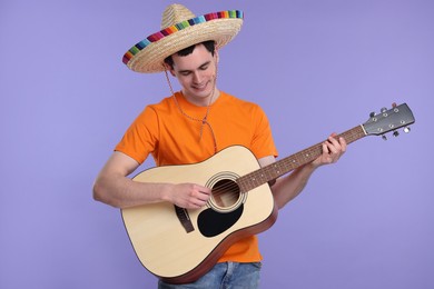 Photo of Young man in Mexican sombrero hat playing guitar on violet background