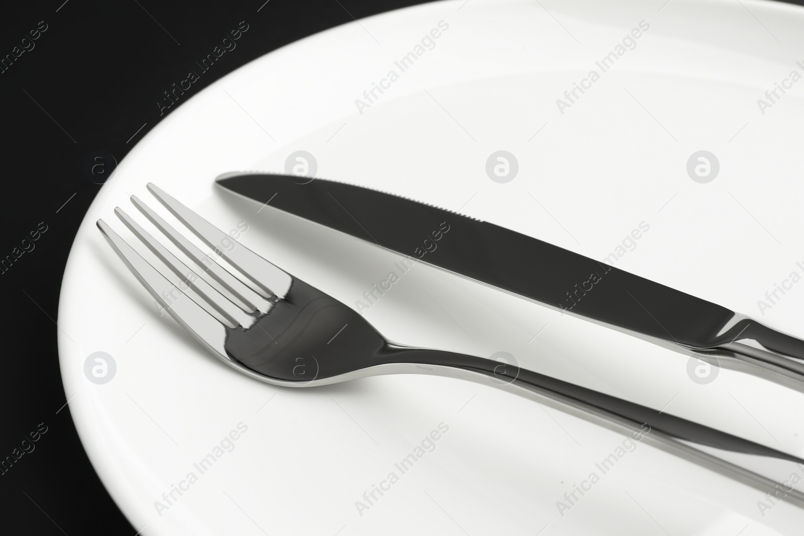 Photo of Clean plate, fork and knife on black table, closeup