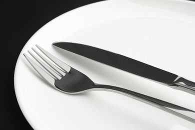 Clean plate, fork and knife on black table, closeup