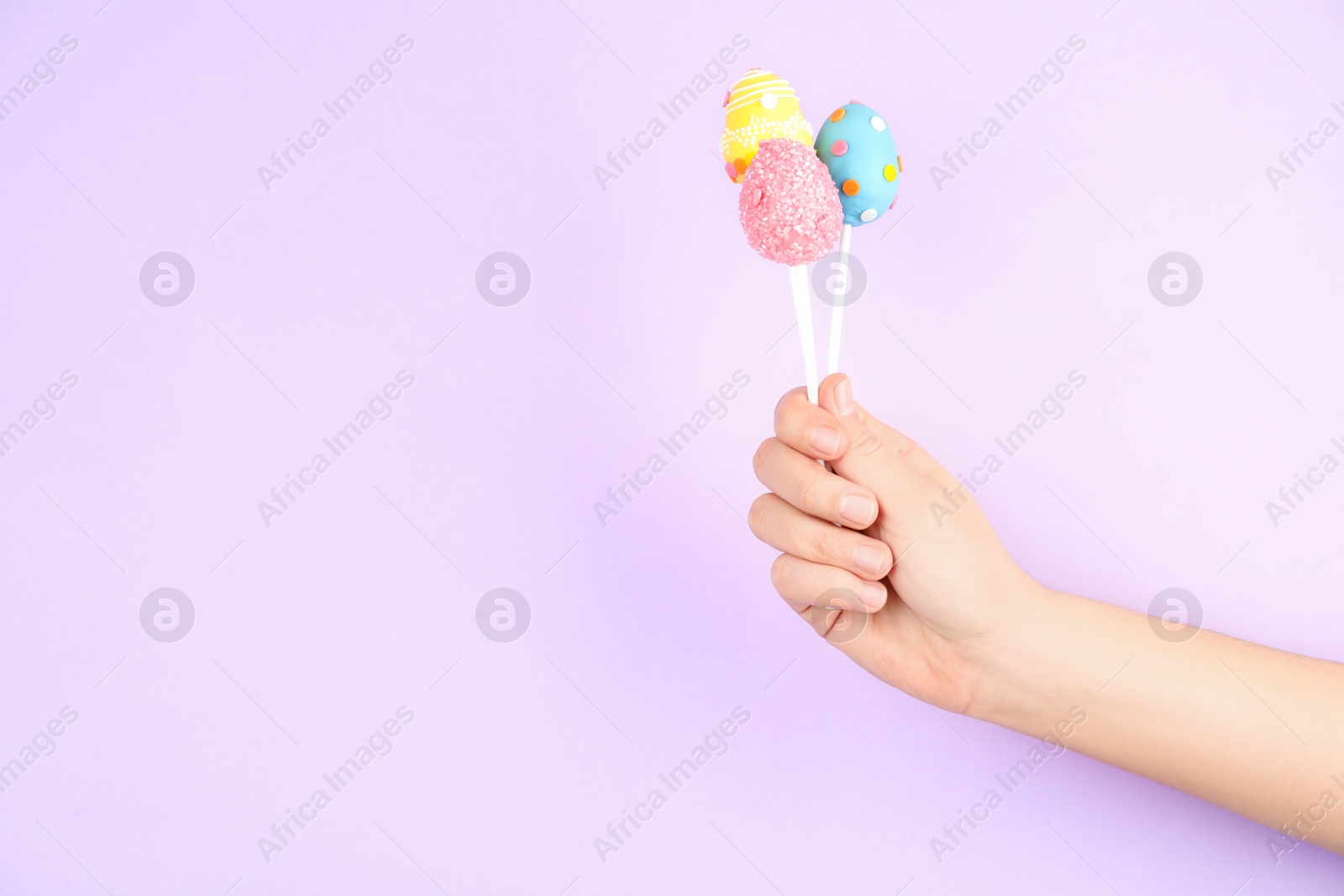 Photo of Closeup view of woman with delicious cake pops on light pink background, space for text. Easter holiday