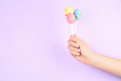 Closeup view of woman with delicious cake pops on light pink background, space for text. Easter holiday