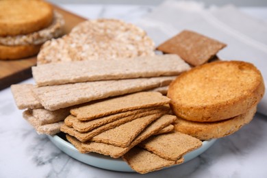 Photo of Plate of rye crispbreads, rice cakes and rusks on white marble table