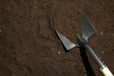 Photo of Metal shovel on fertile soil, top view and space for text. Gardening tool