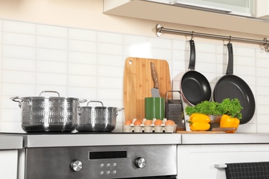 Photo of Set of clean cookware, utensils and products on table in modern kitchen