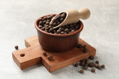 Photo of Aromatic allspice pepper grains in bowl and scoop on grey table