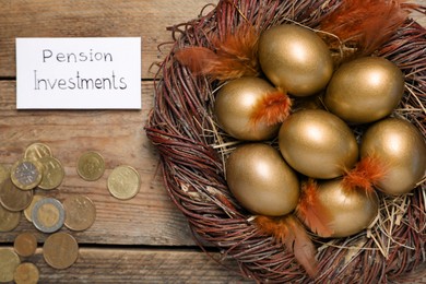 Photo of Many golden eggs, coins and card with phrase Pension Investments on wooden table, flat lay