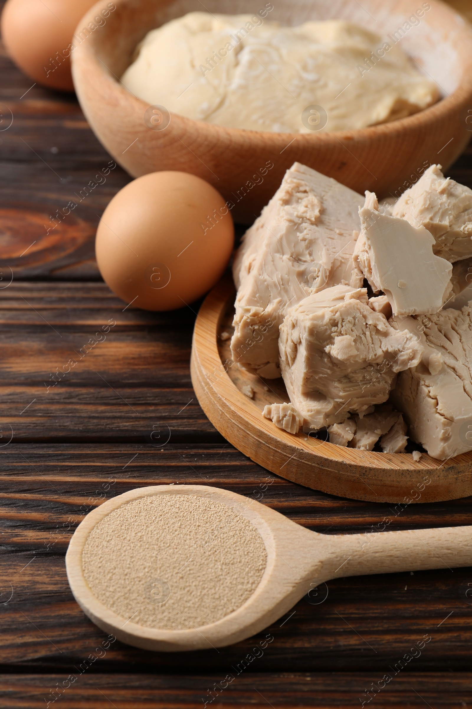 Photo of Compressed and dry granulated yeast, eggs and dough on wooden table