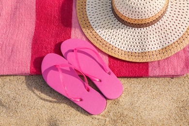 Photo of Beach towel with straw hat and slippers on sand, top view