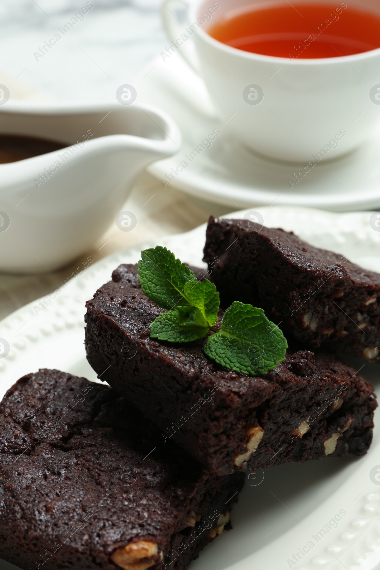 Photo of Delicious brownies with nuts and mint on plate, closeup. Space for text