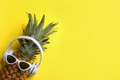 Top view of pineapple with sunglasses and headphones on yellow background, space for text. Creative concept