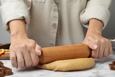 Photo of Woman rolling out dough for cookies at white marble table, closeup