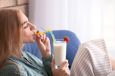 Photo of Young woman with glass of delicious milk shake in armchair indoors