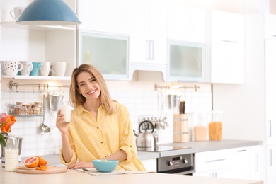 Photo of Beautiful young woman having breakfast and drinking milk in kitchen