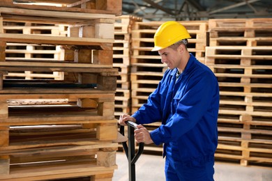 Worker moving wooden pallets with manual forklift in warehouse