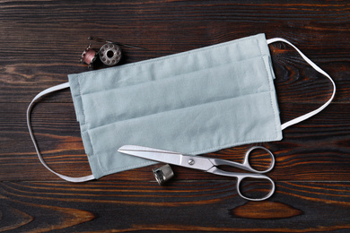 Homemade protective mask and sewing accessories on wooden background, flat lay