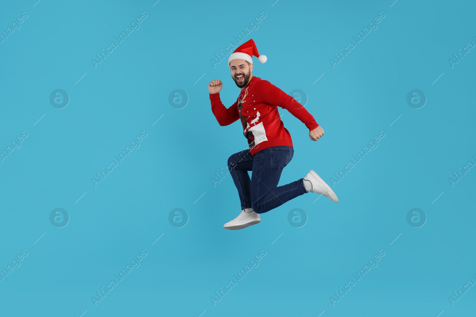 Photo of Happy young man in Christmas sweater jumping on light blue background