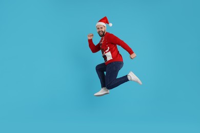 Happy young man in Christmas sweater jumping on light blue background