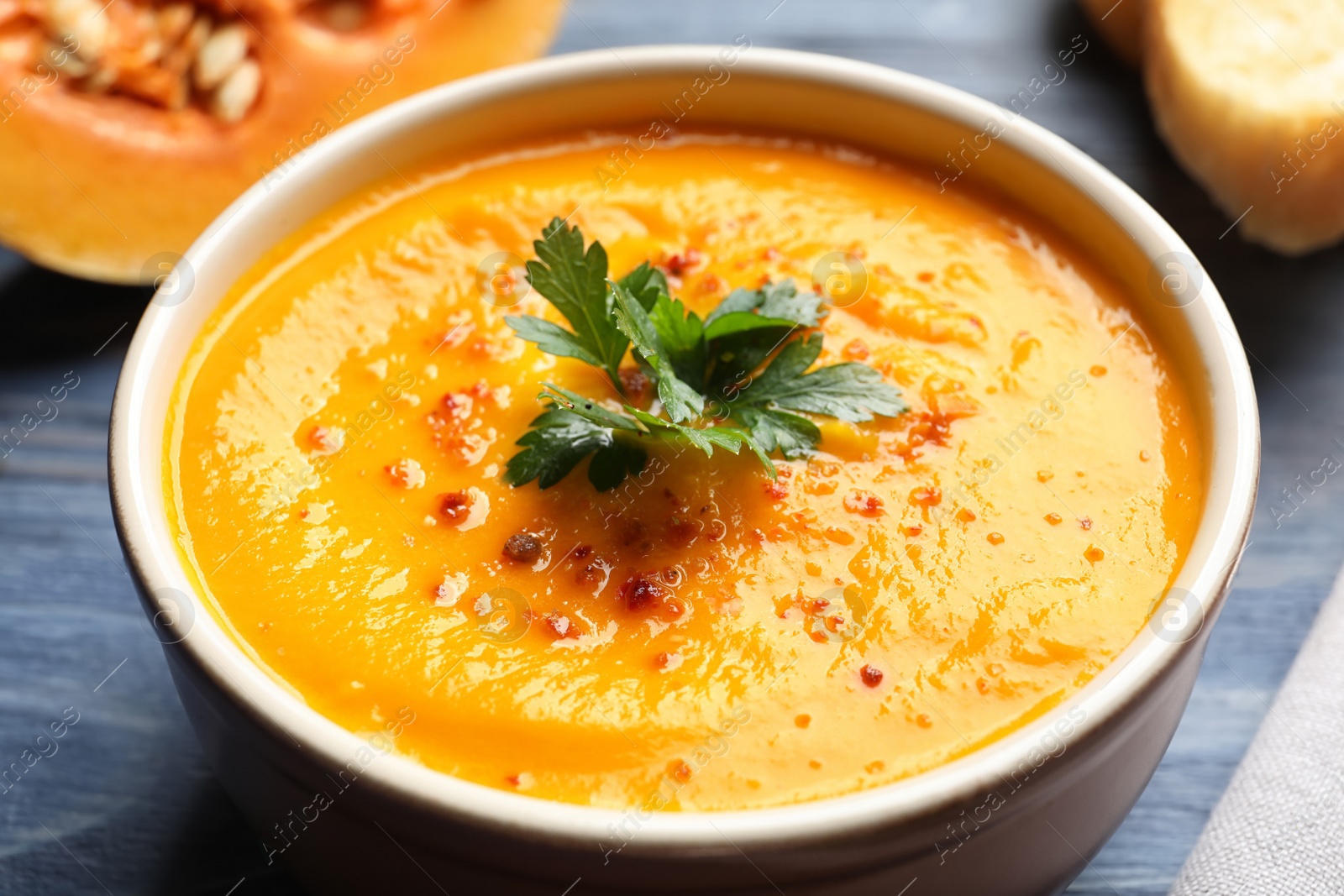 Photo of Delicious pumpkin cream soup with parsley and spices in bowl on table, closeup