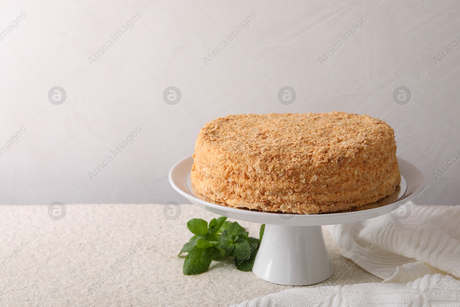 Photo of Delicious Napoleon cake and mint on beige table against light background, space for text