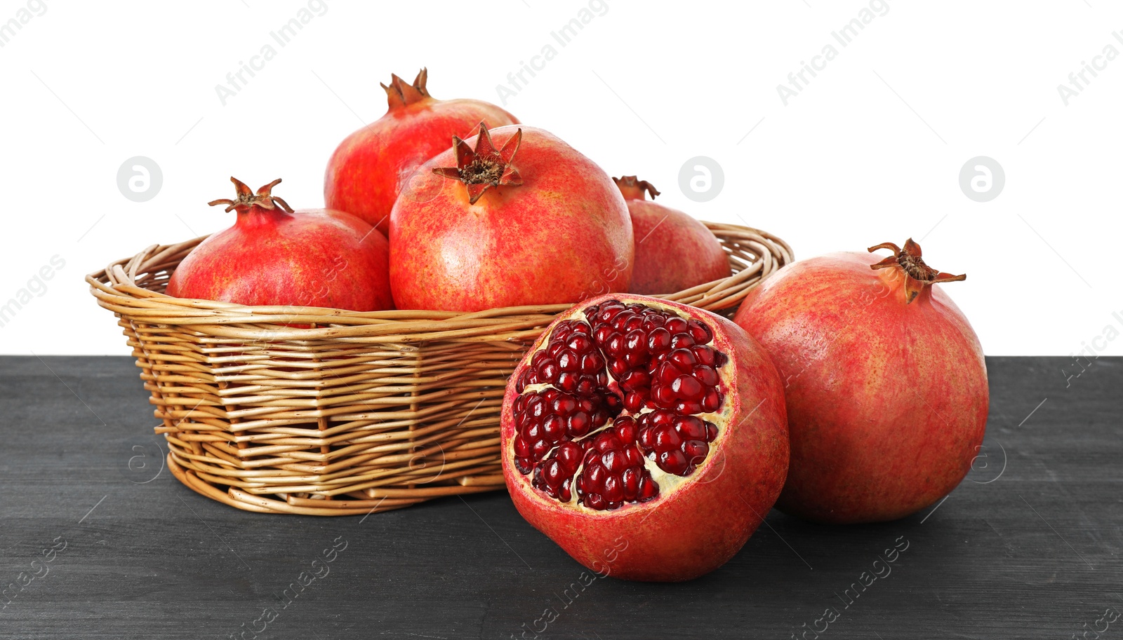 Photo of Fresh pomegranates in wicker basket on black wooden table against white background