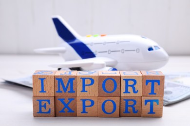 Photo of Words Import and Export made of cubes and toy airplane on white wooden table, closeup