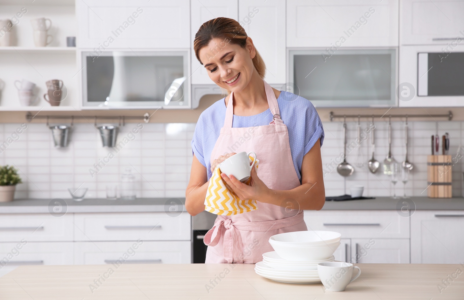 Photo of Woman wiping ceramic cup at table with clean dishes in kitchen