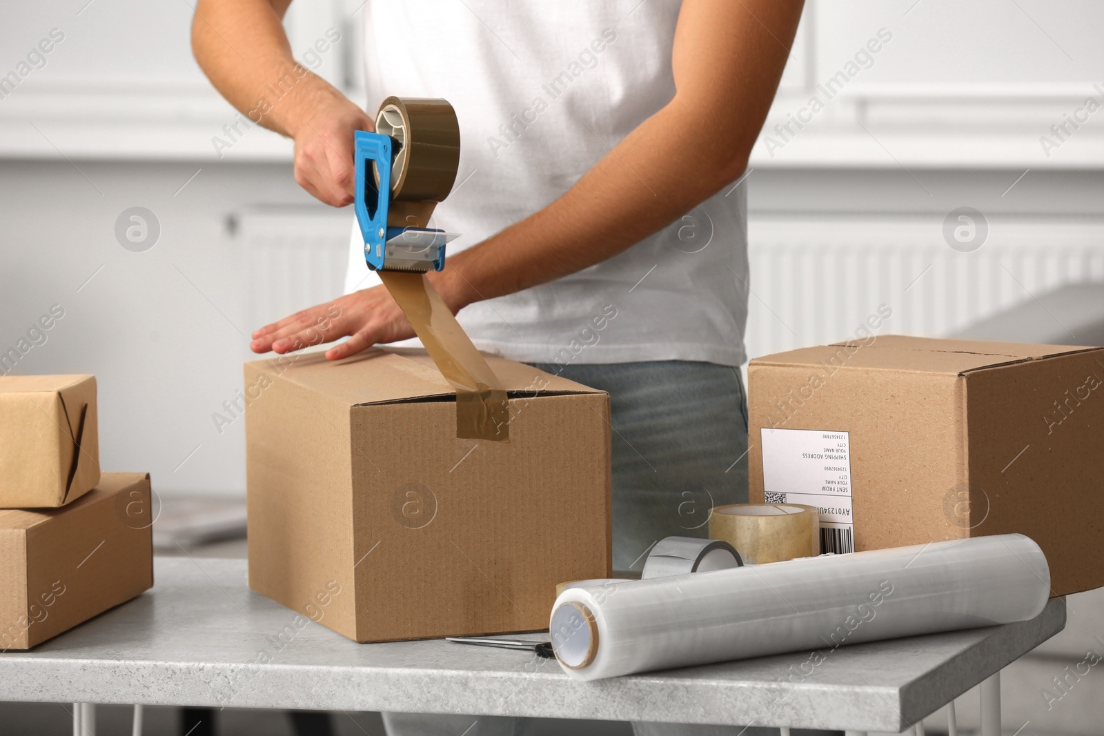 Photo of Man packing box with adhesive tape indoors, closeup