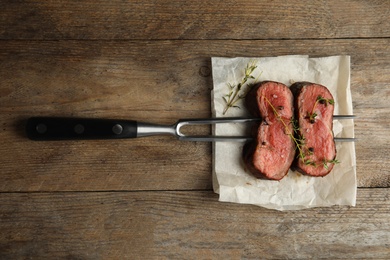 Fork with slices of meat on wooden table, top view